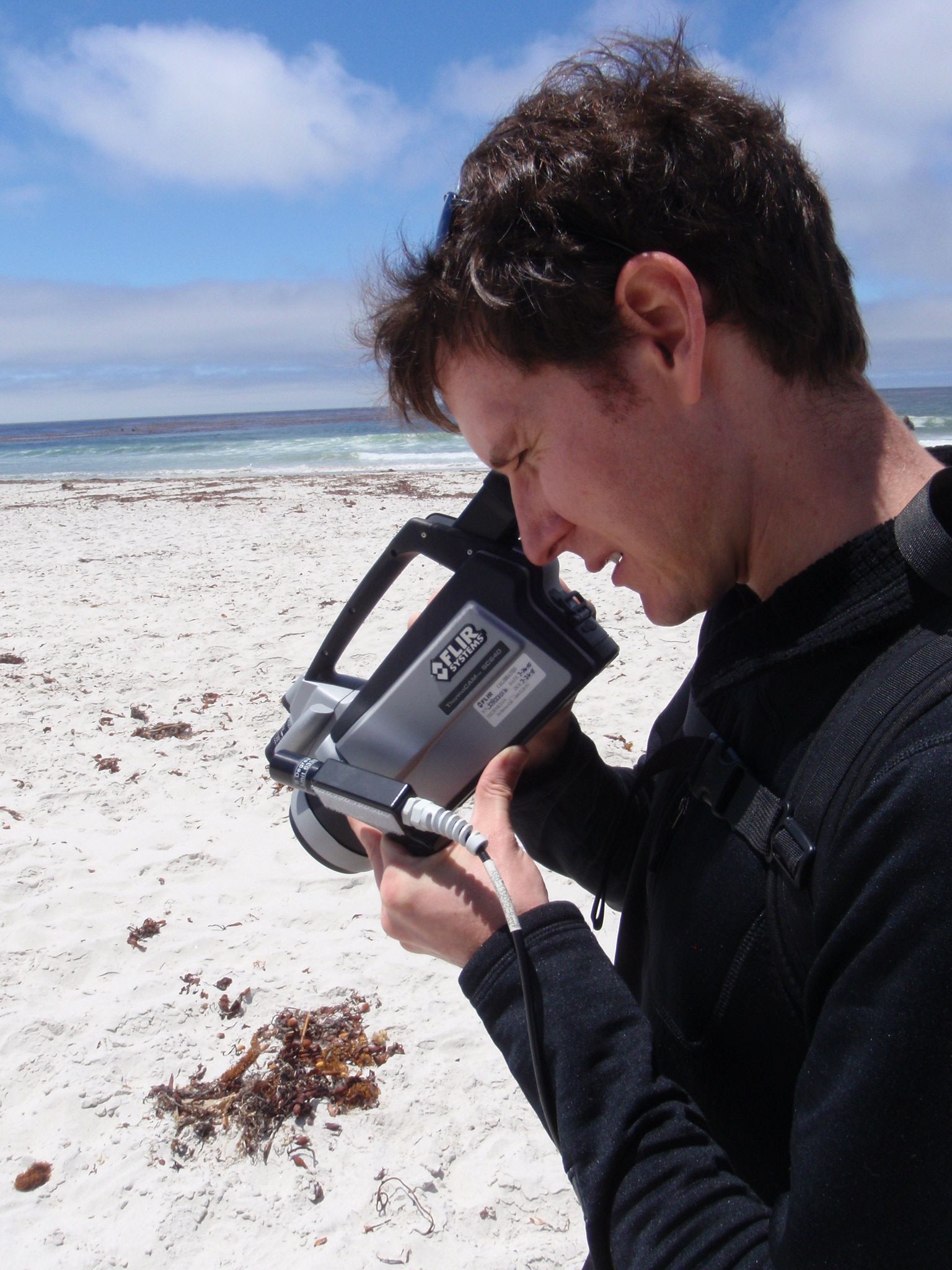 Dr. Chad Brodel uses an infrared camera on a beach in Carmel, CA to determine temperatures as a sensor on an airplane simultaneously collects imagery overhead