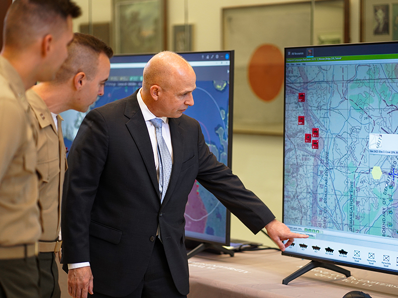 Military personnel discuss a chart displayed on a screen